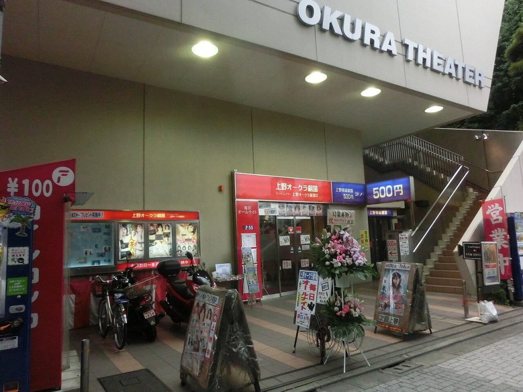 上野仲町通りにある老舗成人映画館「上野オークラ劇場」の外観。白い看板に「OKURA THEATER」の文字、入口にはピンク映画のポスターや「毎日オールナイト」の赤看板、500円の割引表示が並ぶ、昭和レトロな魔境への入り口。